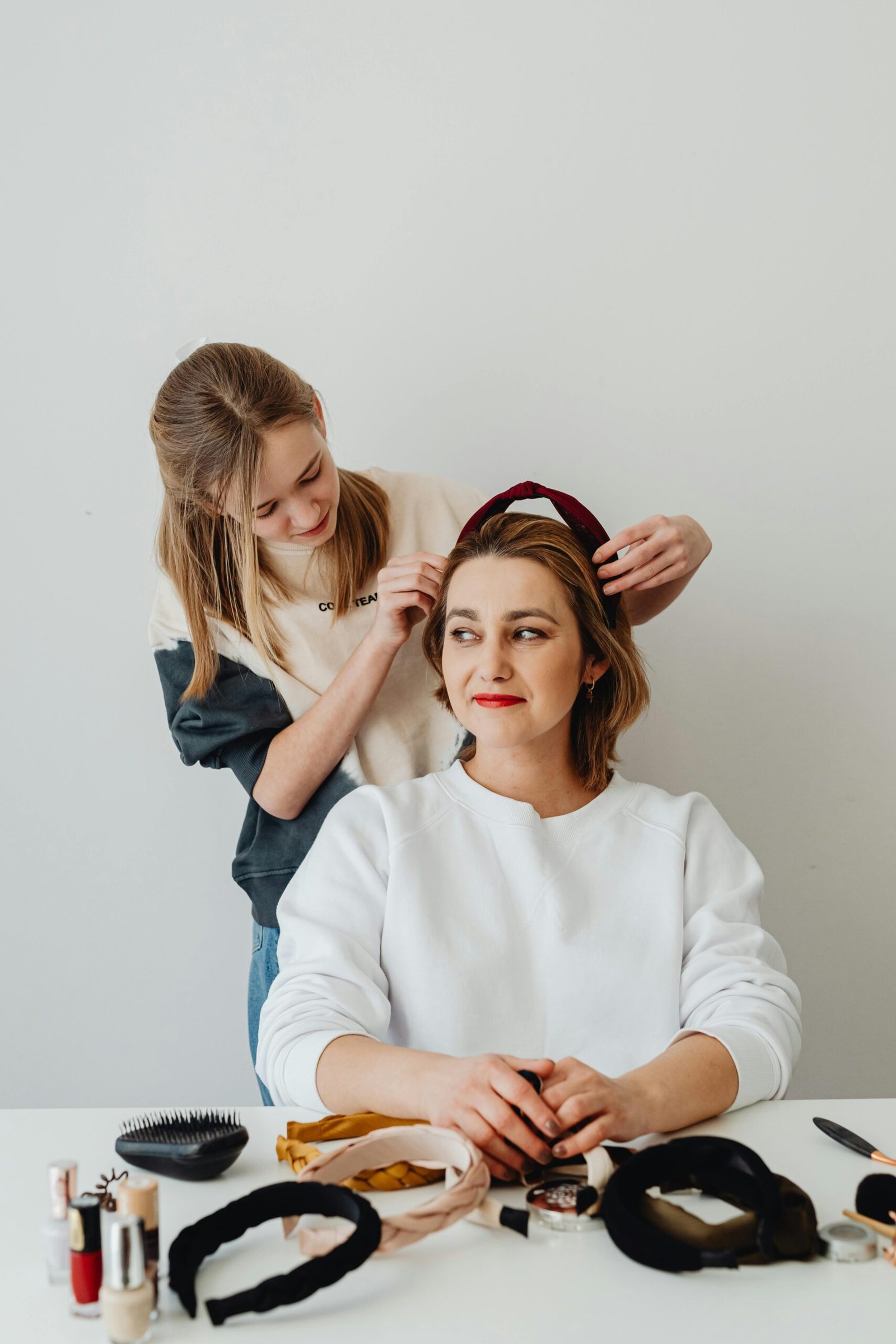 Mother and daughter bonding over hairstyling with headbands at home.